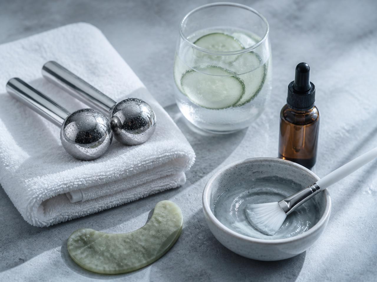 Chilled steel ice globes on a white towel beside a jade tool, serum dropper and bowl of clay mask